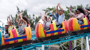 Happy group of people having fun in an amusement park riding on a rollercoaster with arms up
